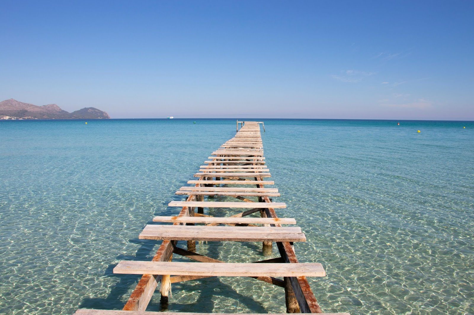 Wooden pier at Playa de Muro in Mallorca, an iconic and most-photographed spot on the island, stretching into the turquoise Mediterranean Sea.