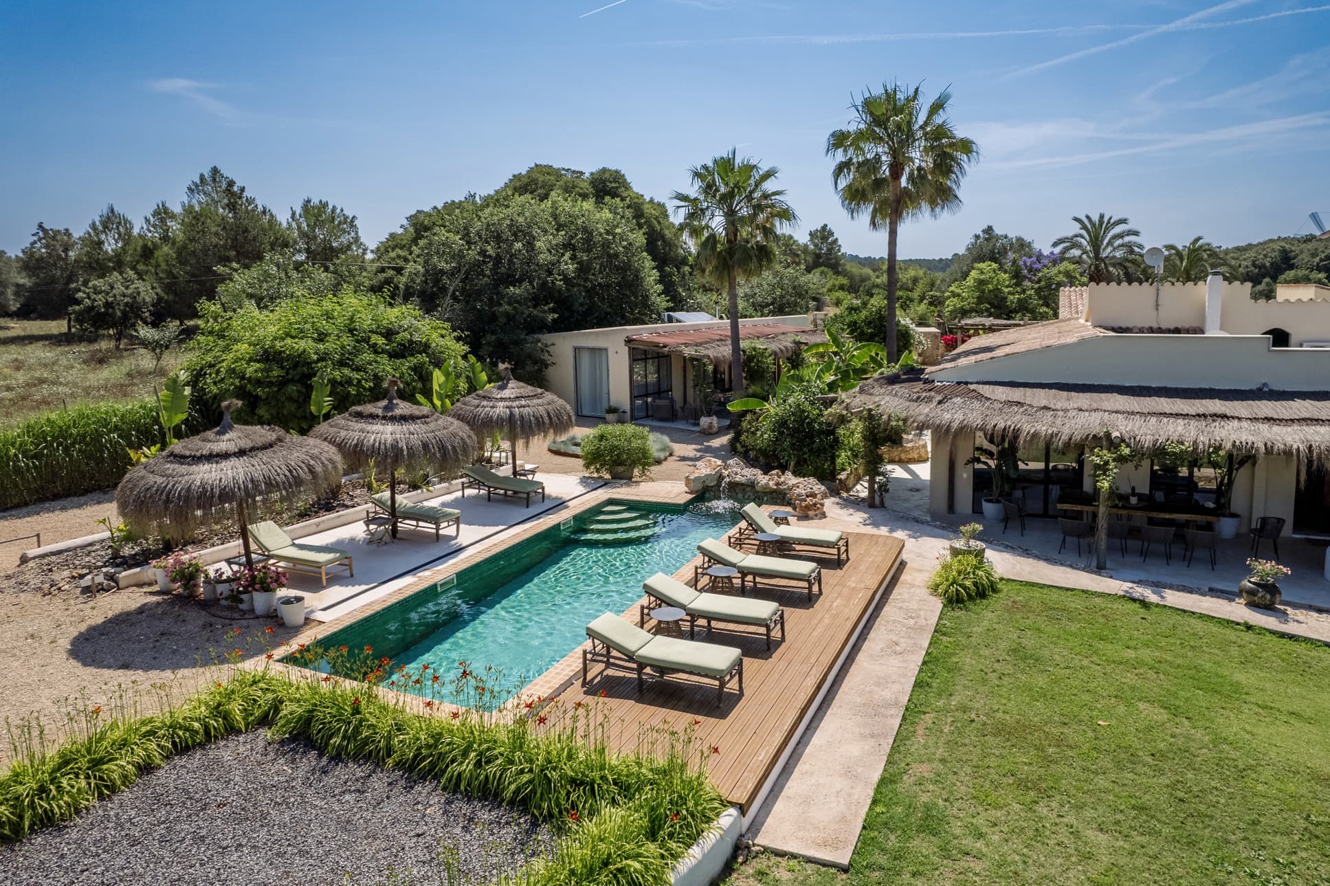 Serena villa de lujo en Llubí con piscina privada, tumbonas y un exuberante jardín bajo palmeras.