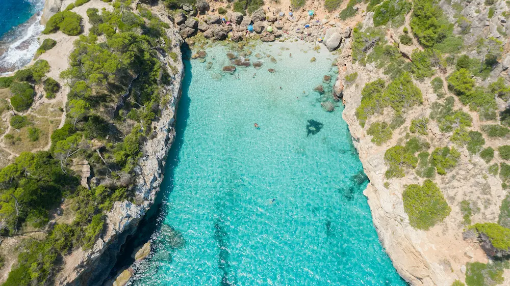 Crystal-clear turquoise water at Caló des Moro in Santanyí, Mallorca, surrounded by steep cliffs and Mediterranean pine trees, showcasing one of the island’s best hidden coves.