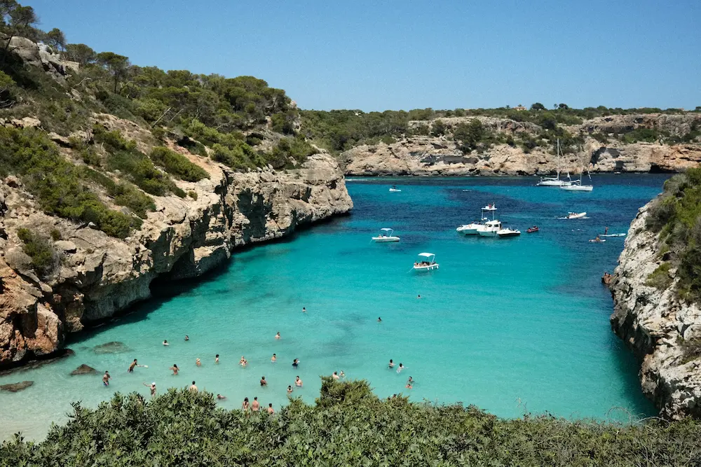 Scenic turquoise bay in Mallorca with yachts and swimmers, showcasing the natural beauty and appeal of luxury tourism Mallorca.