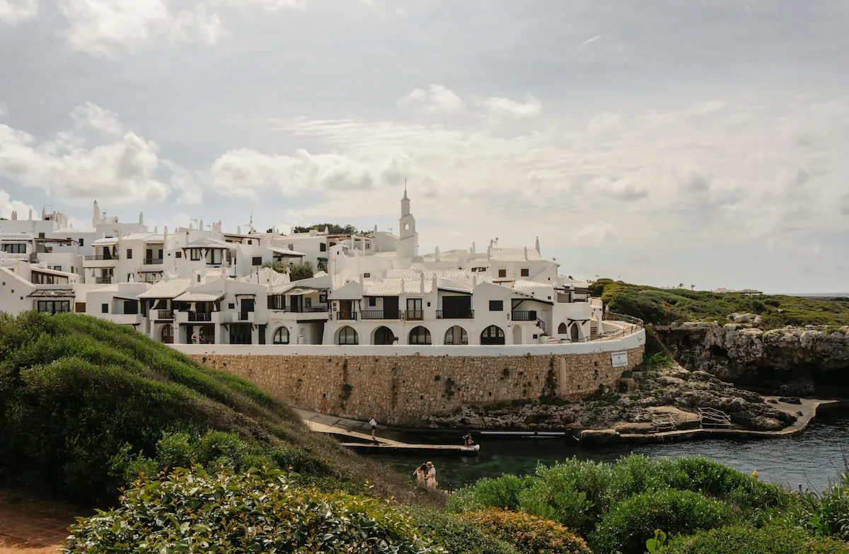 Vista de la costa de Ciutadella Menorca con villas blancas en los acantilados sobre el mar, mostrando una de las zonas a tener en cuenta a la hora de decidir dónde alojarse en Ciutadella Menorca